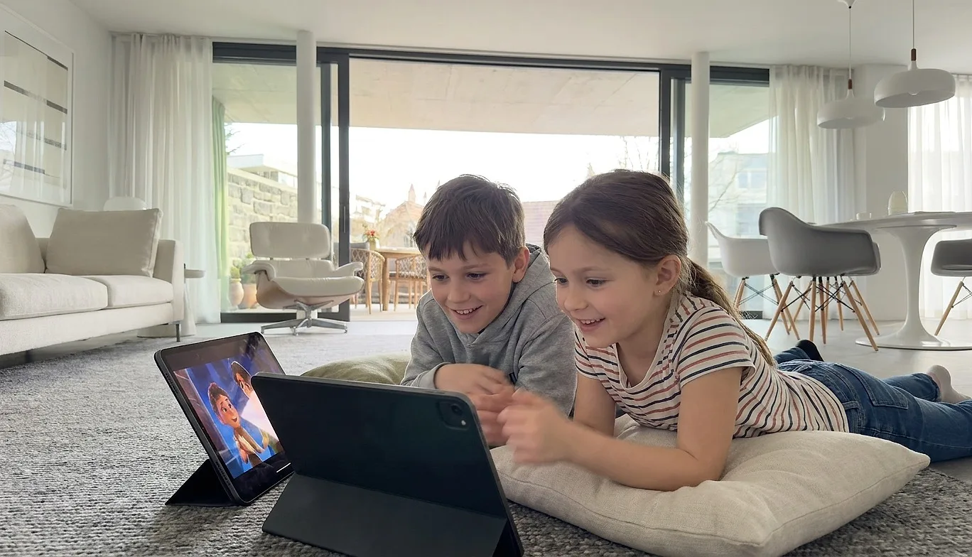 Two children watching a cartoon on a tablet in the living room
