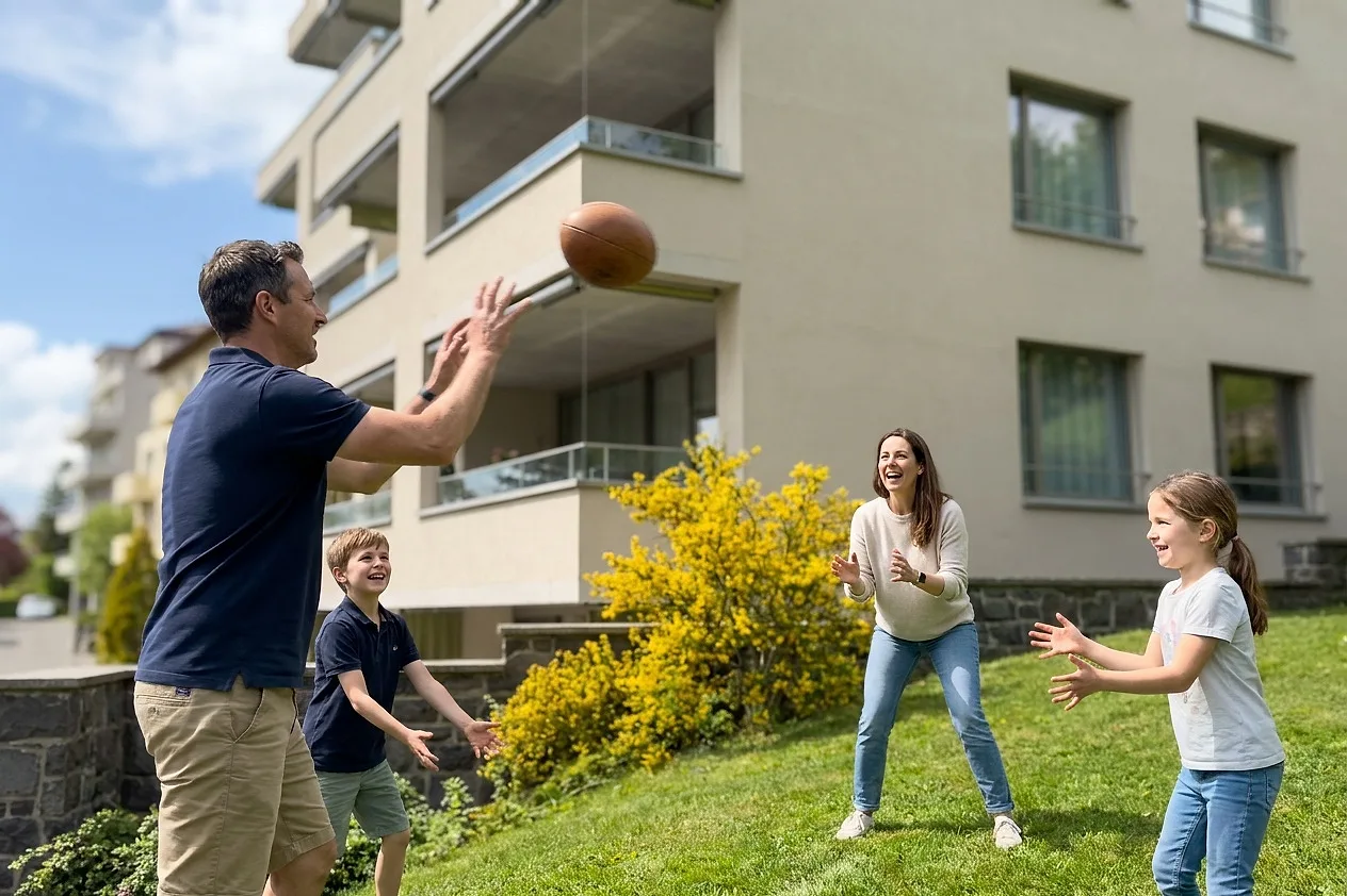 A family playing ball on the lawn below the building