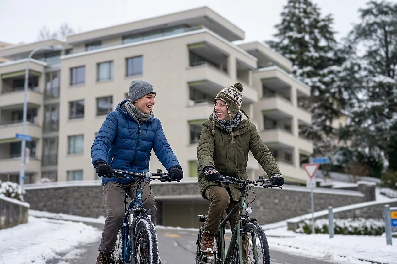 Two teenagers cycling past the building in the snow
