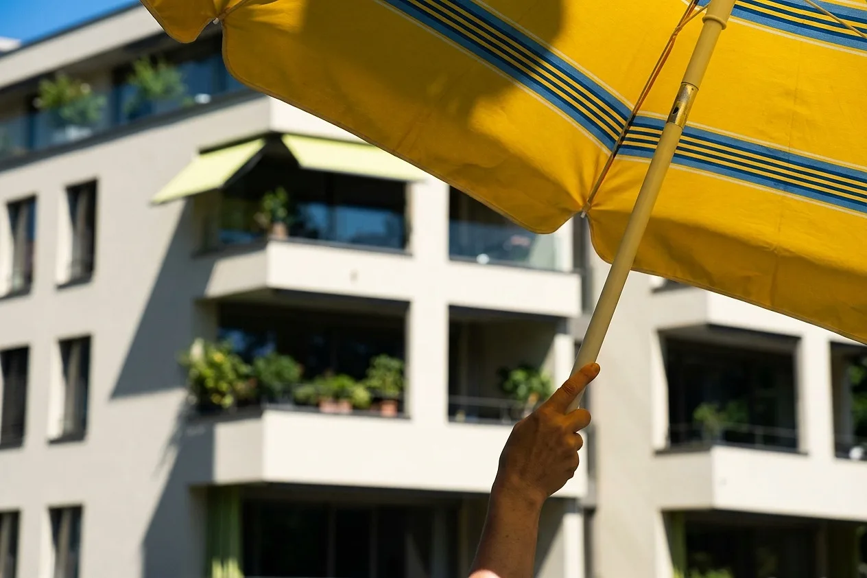 A yellow parasol held up against the facade in summer